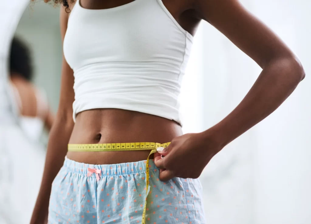 adult woman measures waistline with tape measure utc
